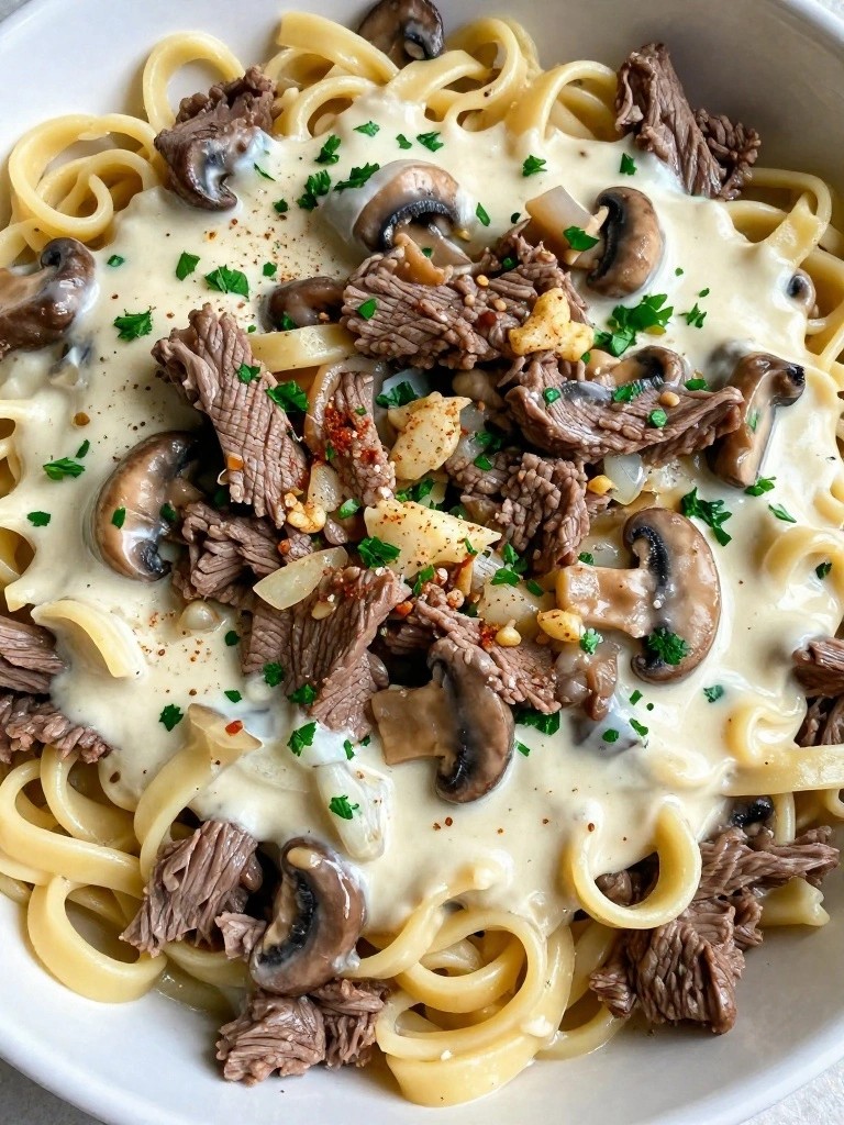 Creamy fettuccine pasta topped with sliced beef, mushrooms, and herbs.