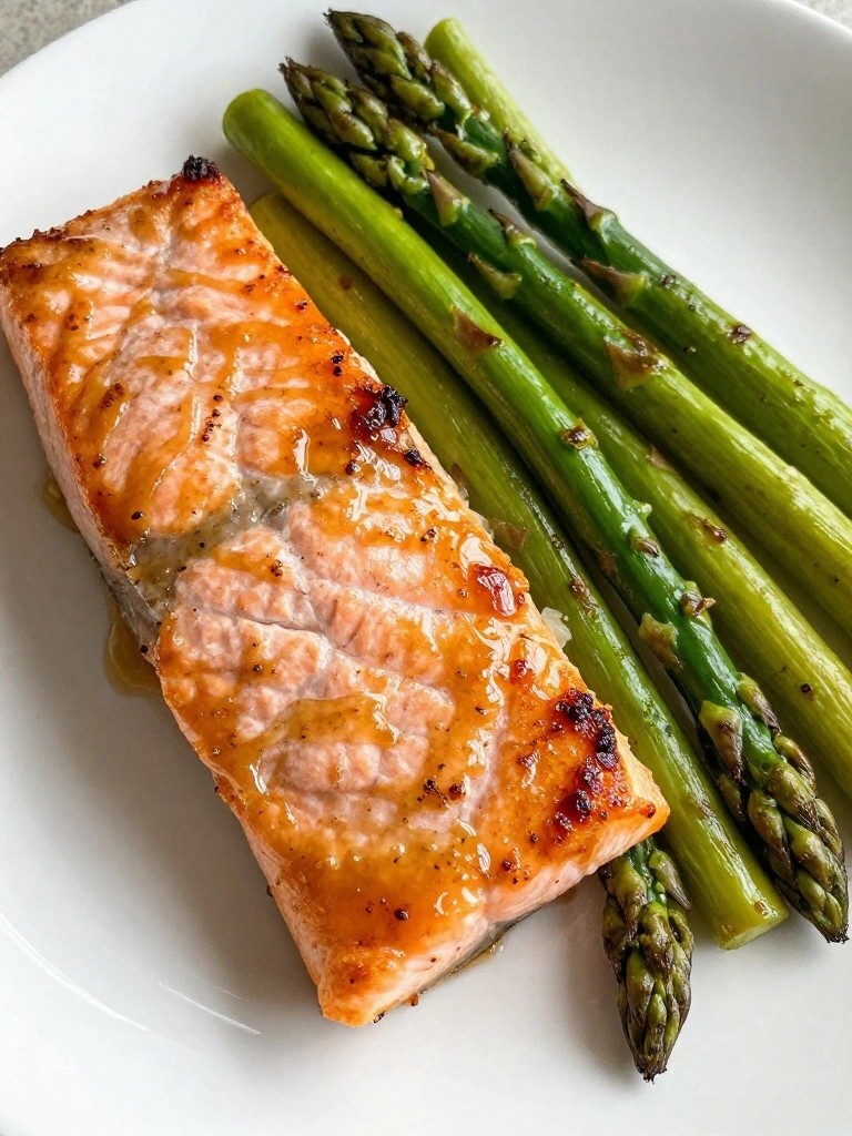 Seared salmon fillet with glossy glaze beside grilled asparagus spears.