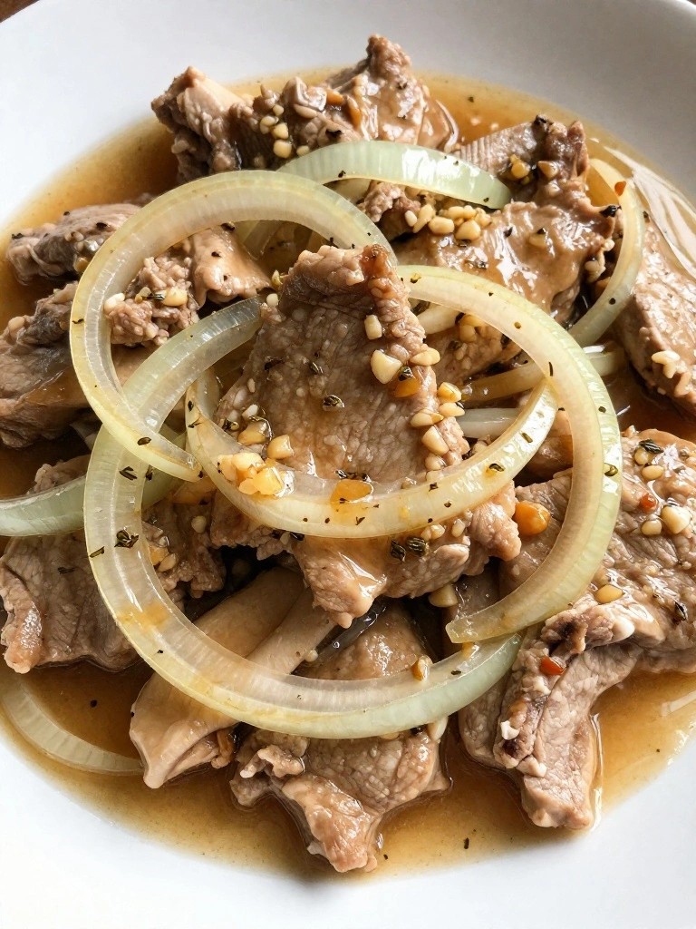 Sliced meat and onion rings in light brown sauce with garlic.