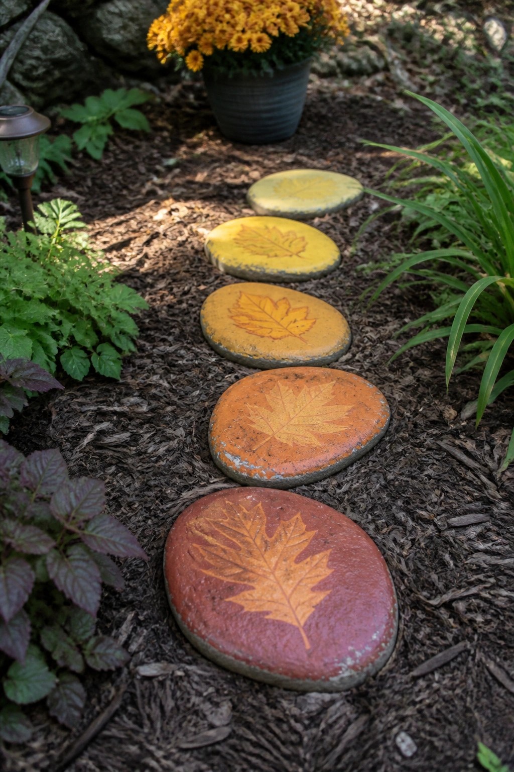 Painted leaf stepping stones in yellow, orange, and red on a garden path.