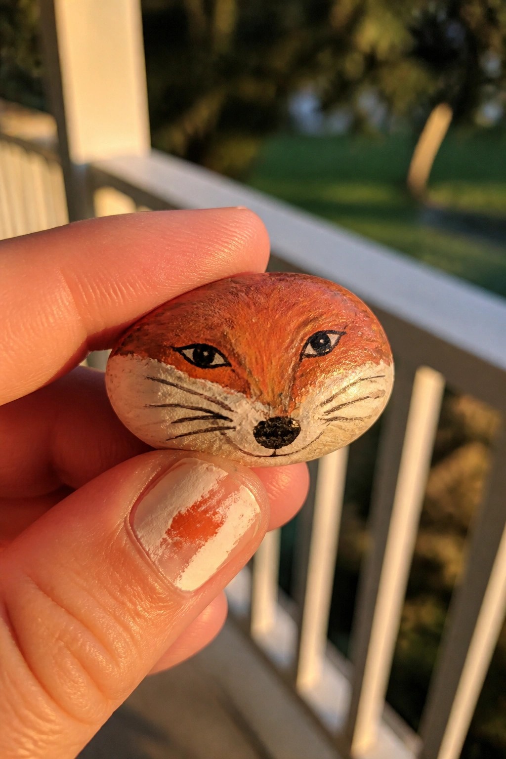 Hand holding orange fox-faced rock, white muzzle, black details, paint on thumb