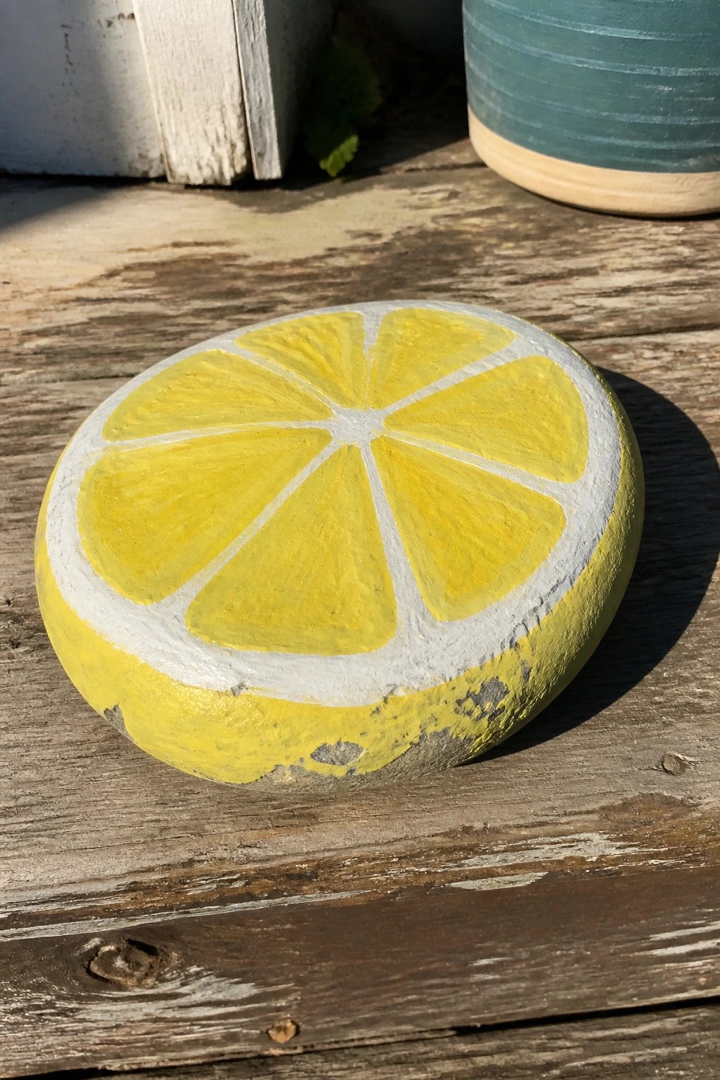 Round rock painted as yellow lemon slice on weathered wooden planks