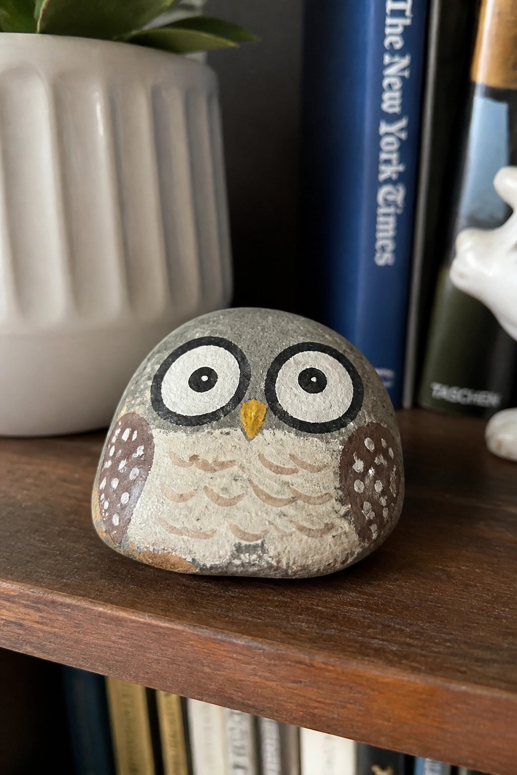 Painted rock owl with large eyes and dotted wings on wooden shelf