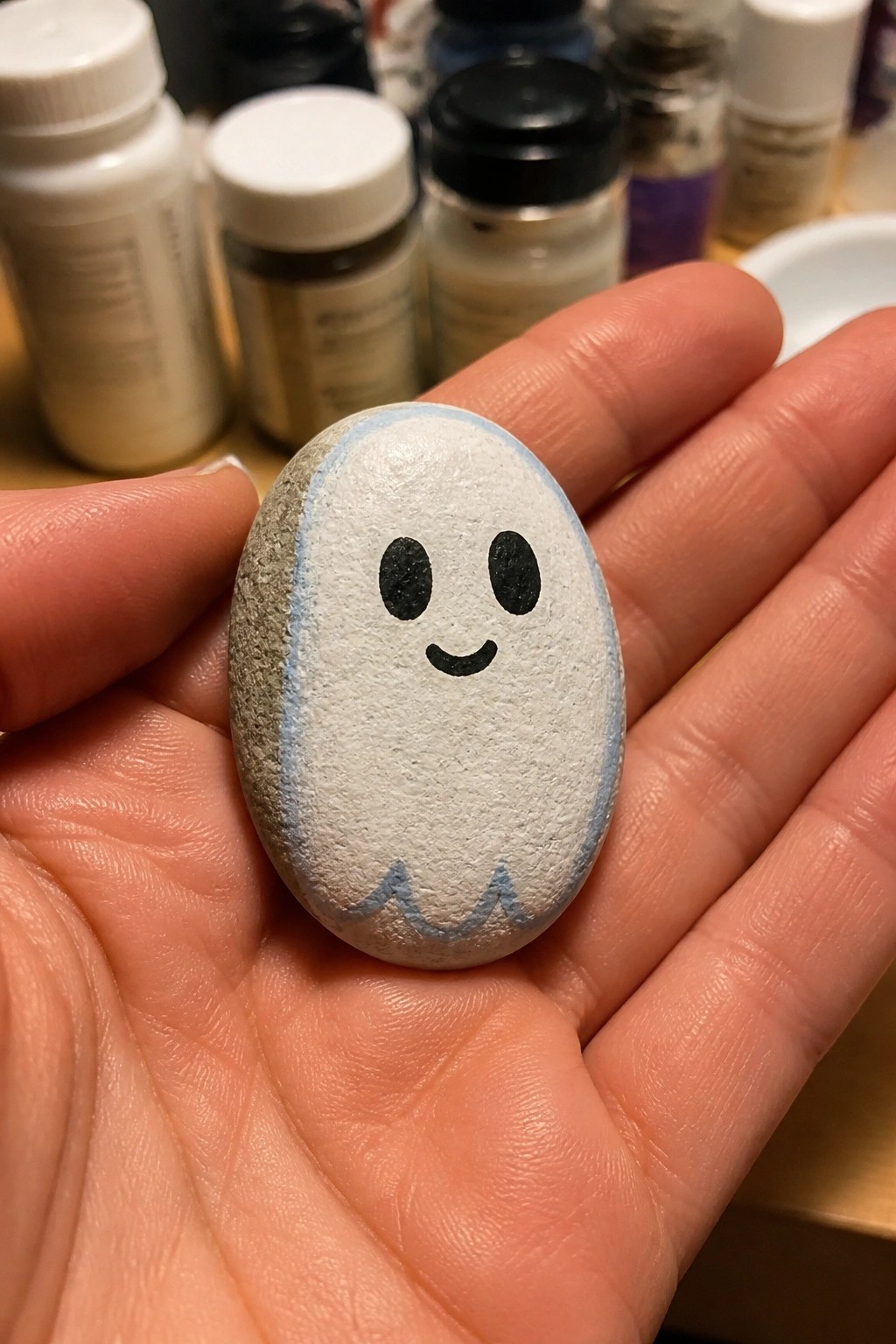 Hand holding oval white ghost rock with black eyes and blue trim