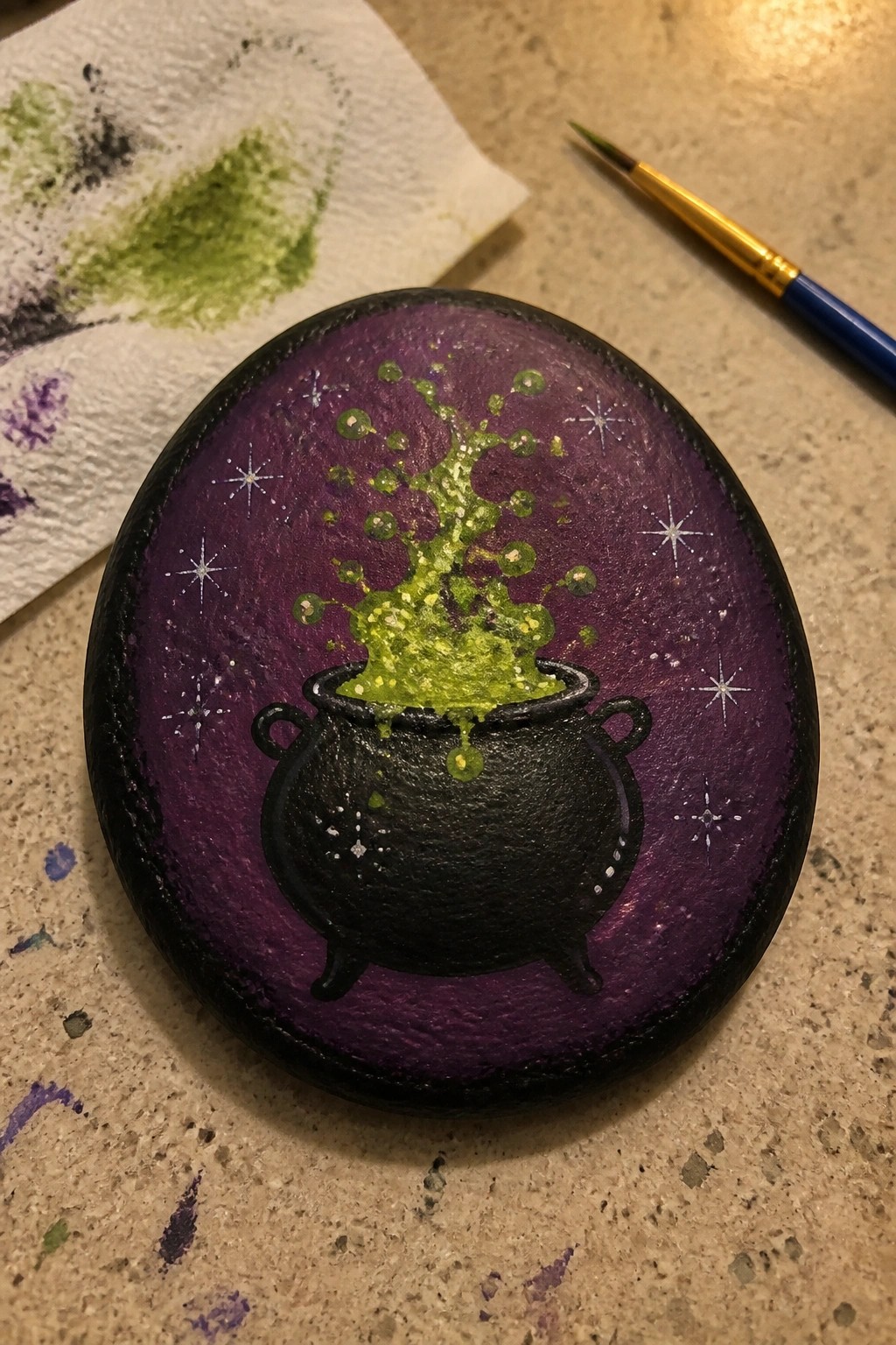 Black cauldron with green bubbling potion on purple starry painted rock