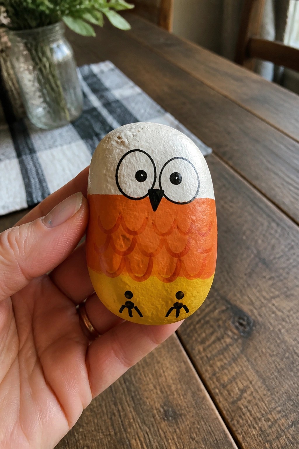 Hand holding painted owl rock with white head, orange feathers, yellow base