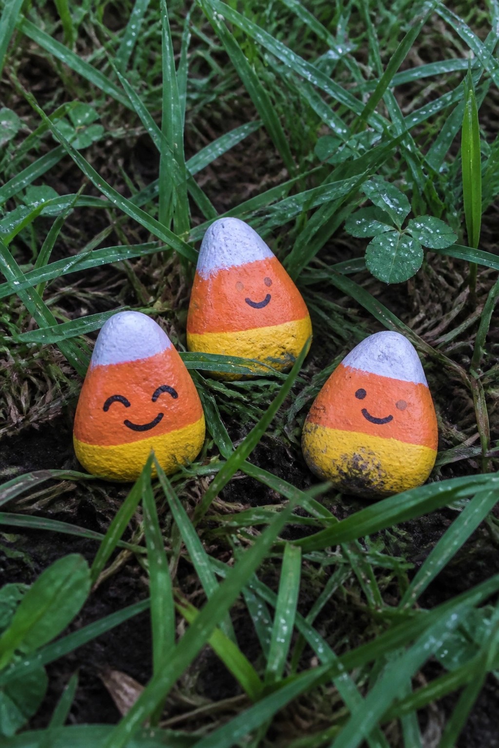 Three painted candy corn rocks with smiling faces in green grass