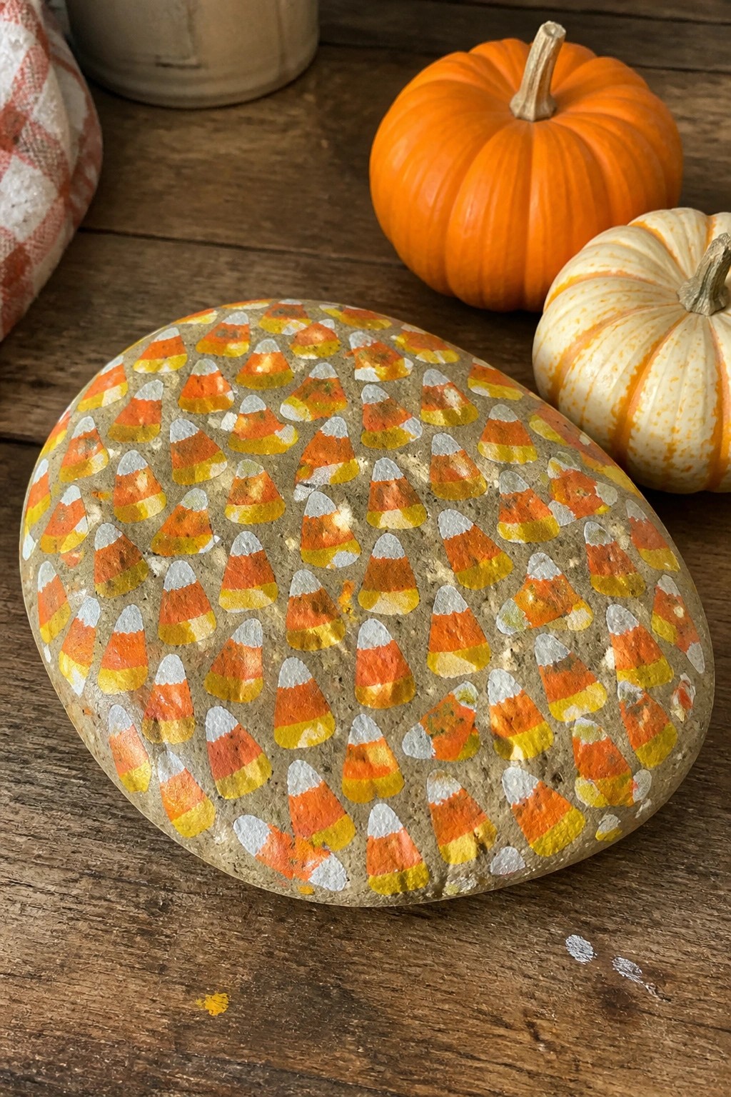 Painted rock with candy corn pattern beside pumpkins on wooden table