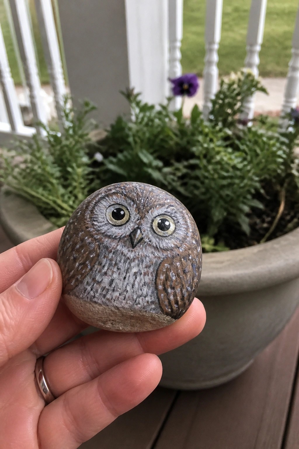 Hand holding painted stone owl with brown-gray feathers and large eyes