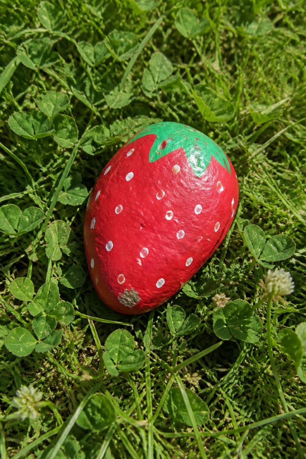 Red strawberry-painted rock with white dots and green top on grass