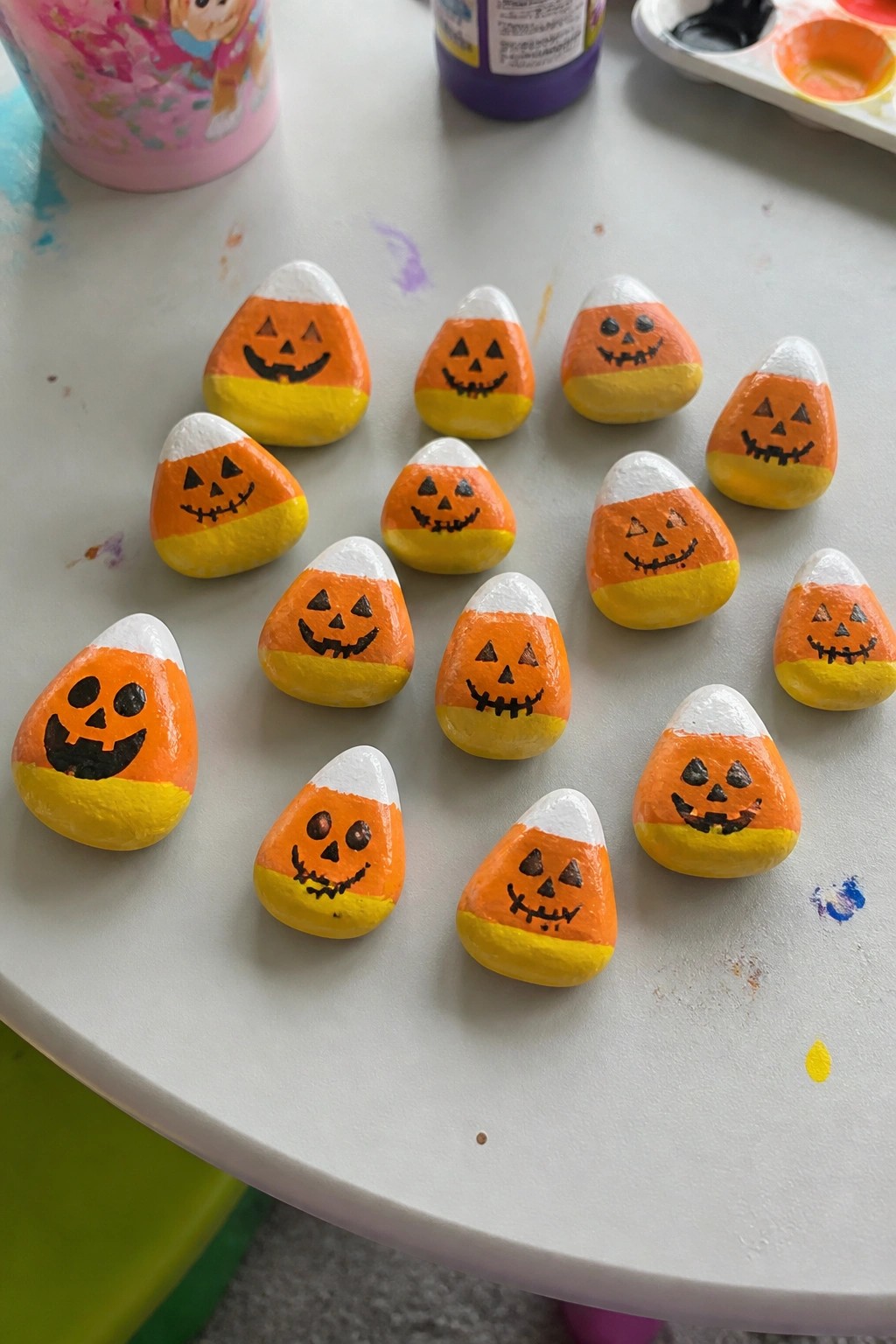 Hand-painted candy corn rocks with jack-o'-lantern faces on white table