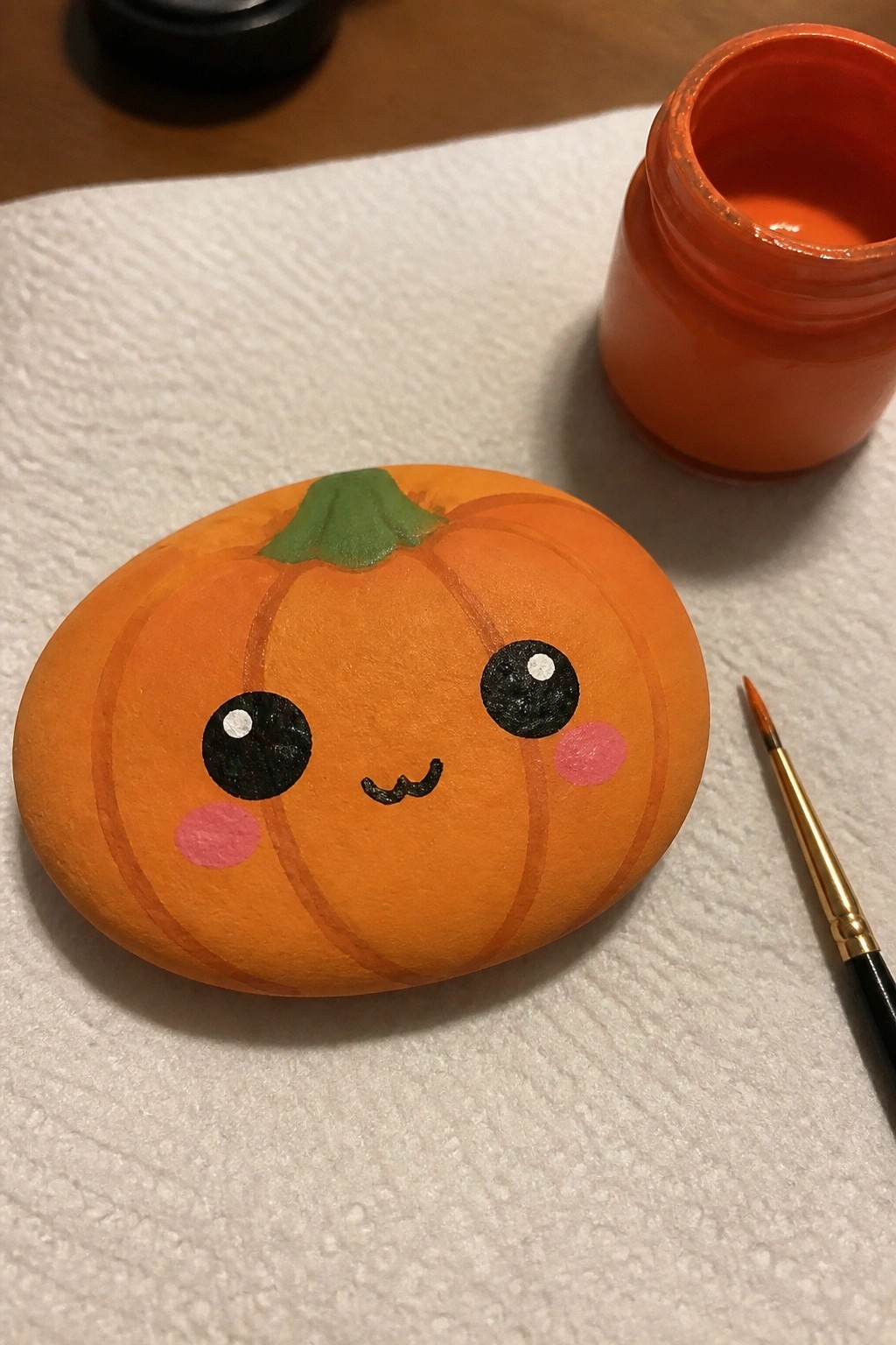 Cute orange pumpkin face painted on rock beside paint jar and brush