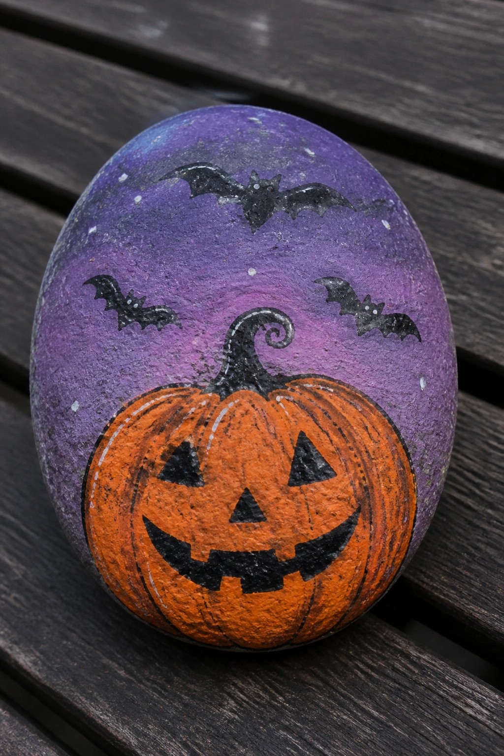 Painted purple rock with orange jack-o'-lantern, black bats, and starry sky