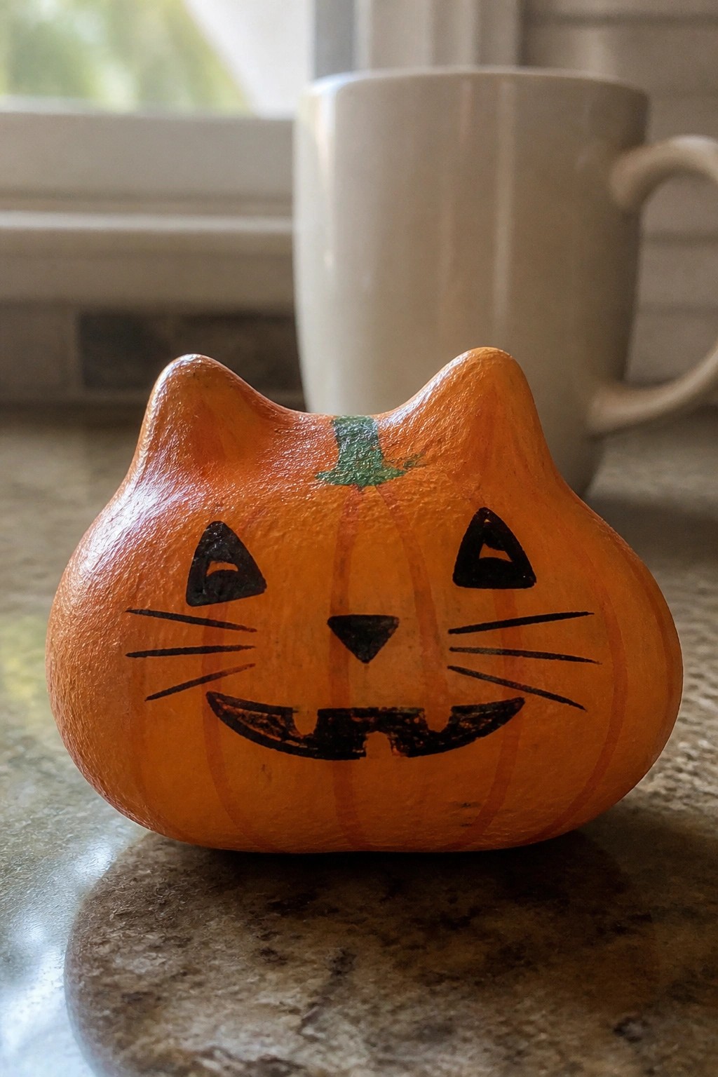 Wooden orange cat pumpkin with painted black jack-o'-lantern face on countertop.
