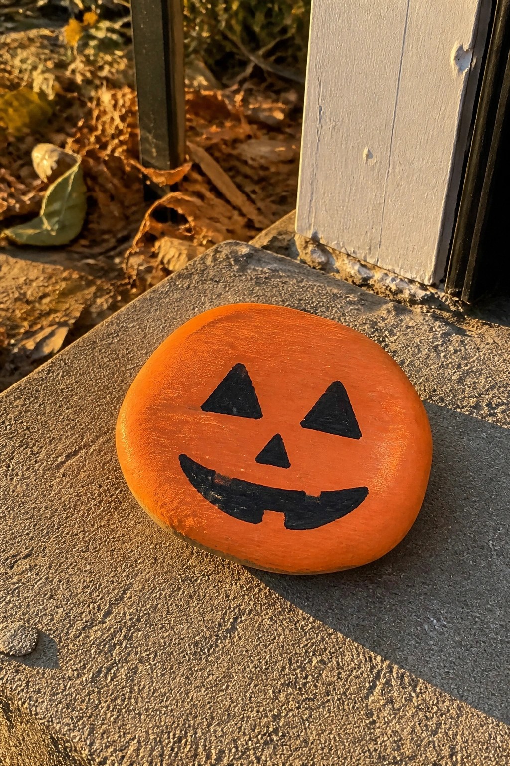 Orange jack-o'-lantern painted rock on concrete step by white door frame