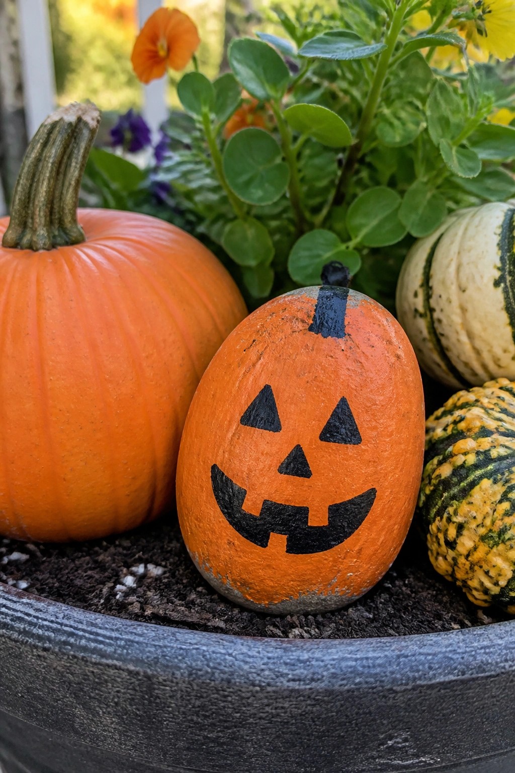 Painted jack-o'-lantern among orange pumpkin, striped gourds, and autumn plants in pot