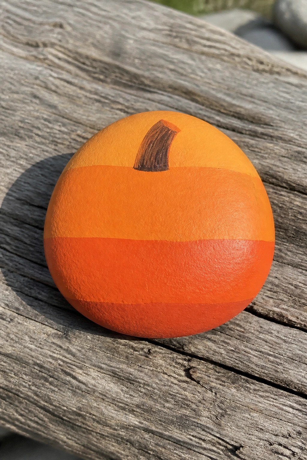 Orange pumpkin-painted rock with brown stem on weathered wooden planks