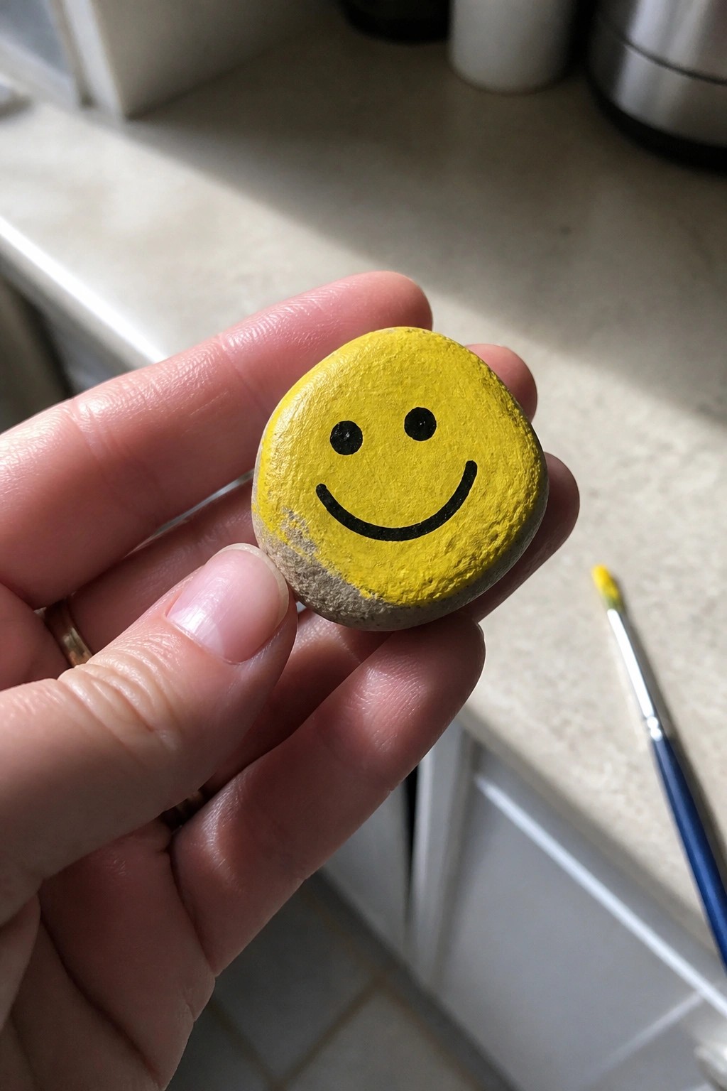 Hand holding small yellow smiley face painted on round stone