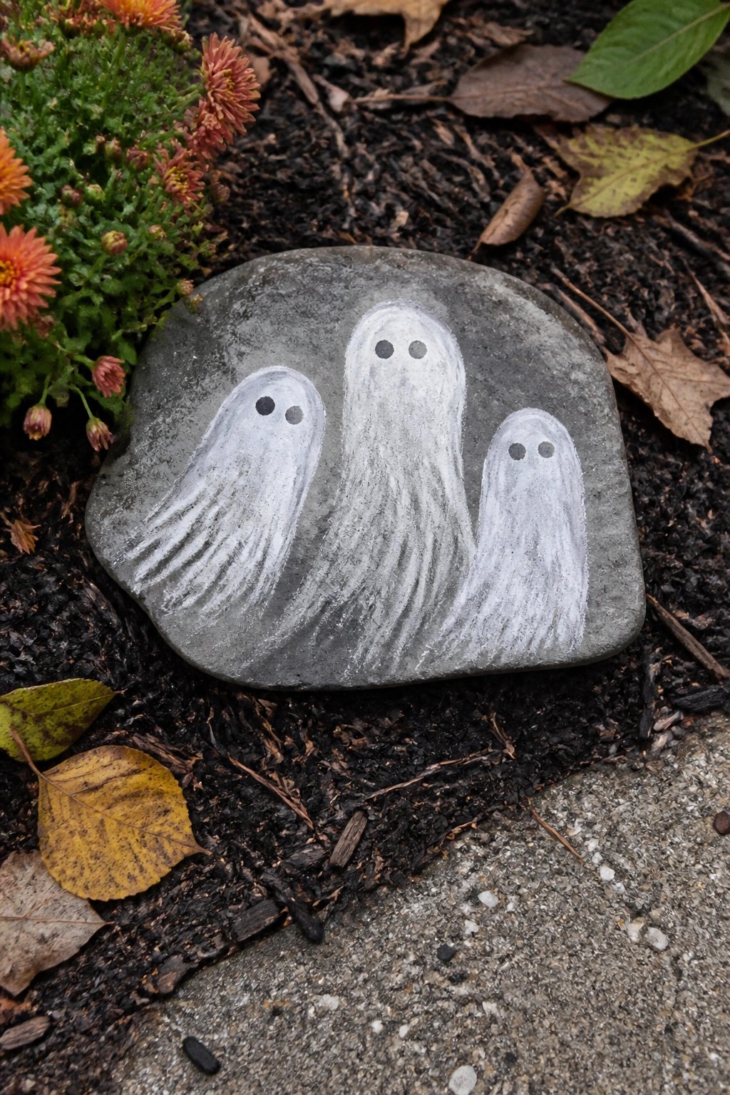 Three white ghosts painted on gray rock amid leaves and soil