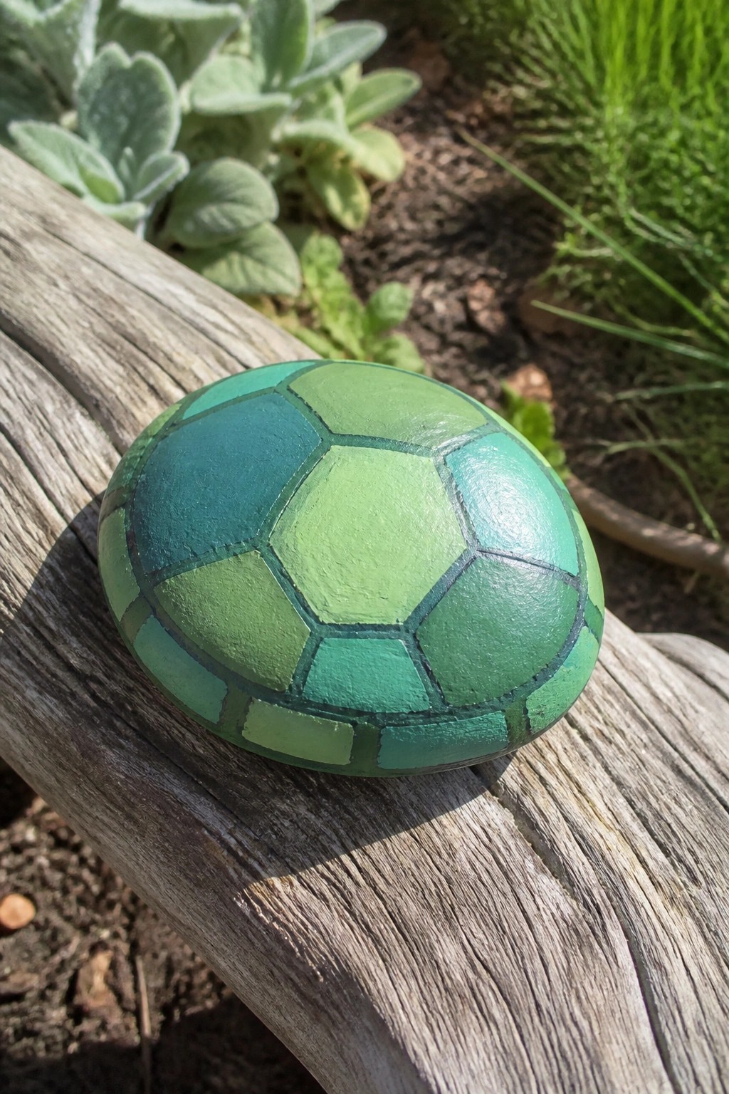 Green painted rock with turtle shell pattern on weathered wooden beam outdoors