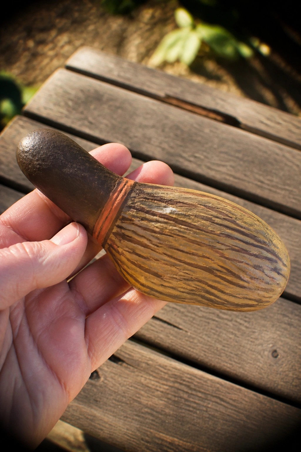 Hand holding miniature wooden bowling pin with dark top and orange band