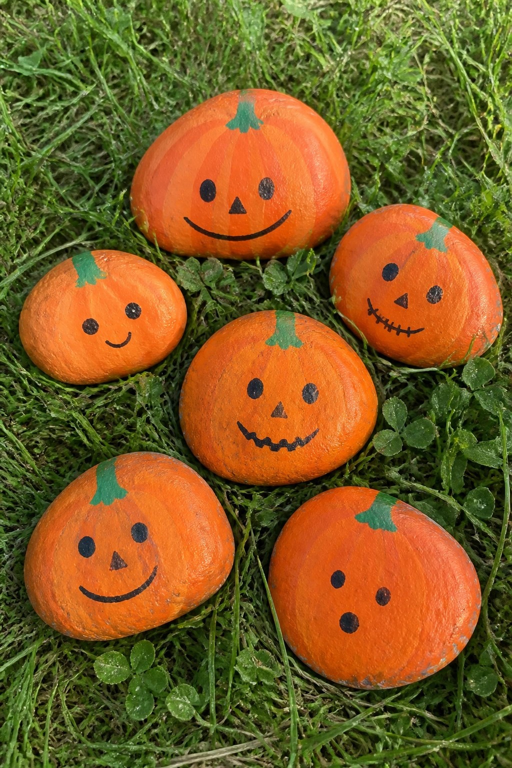 Six orange painted rocks with jack-o'-lantern faces on green grass