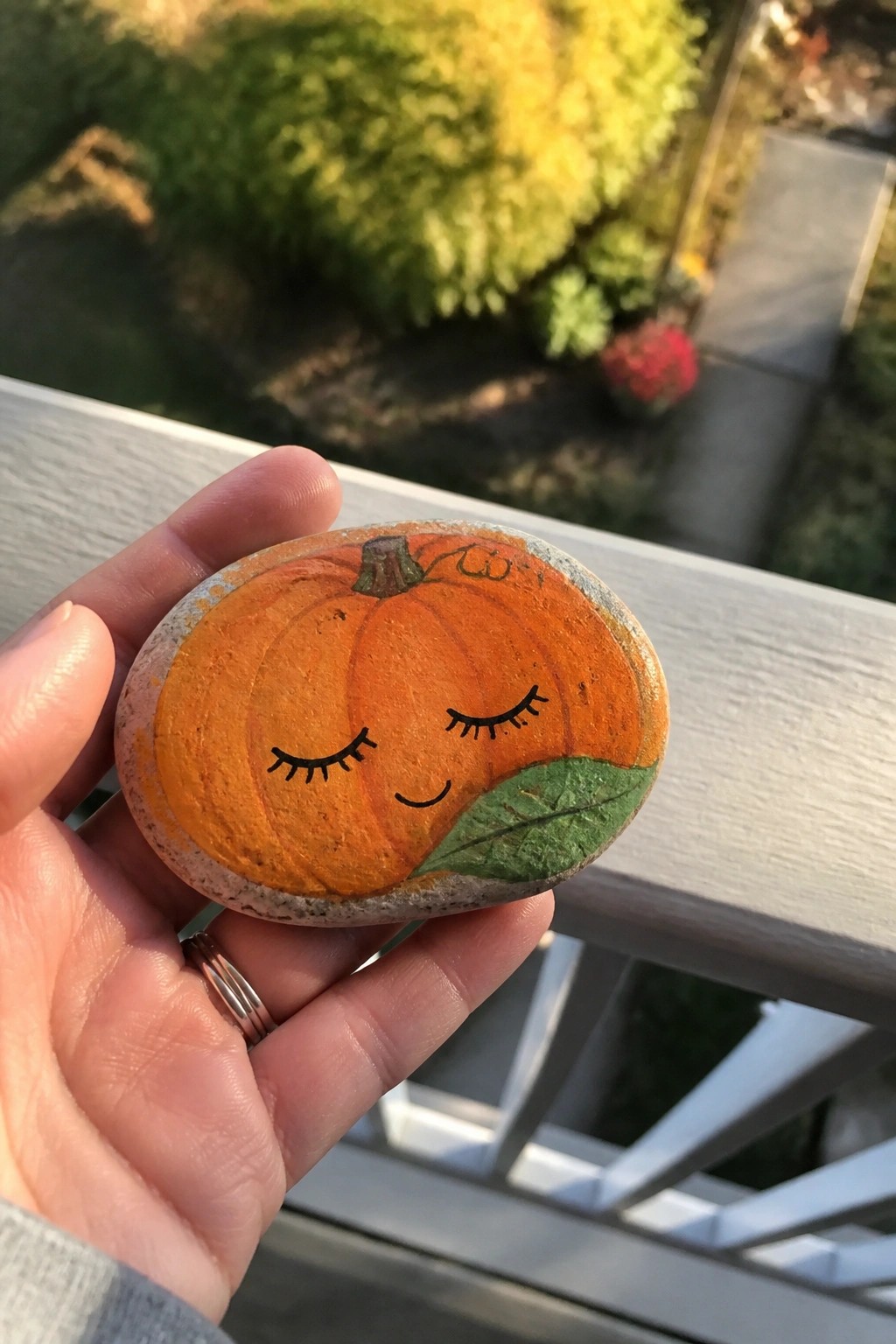 Hand holding painted orange pumpkin rock with closed eyes and green leaf.