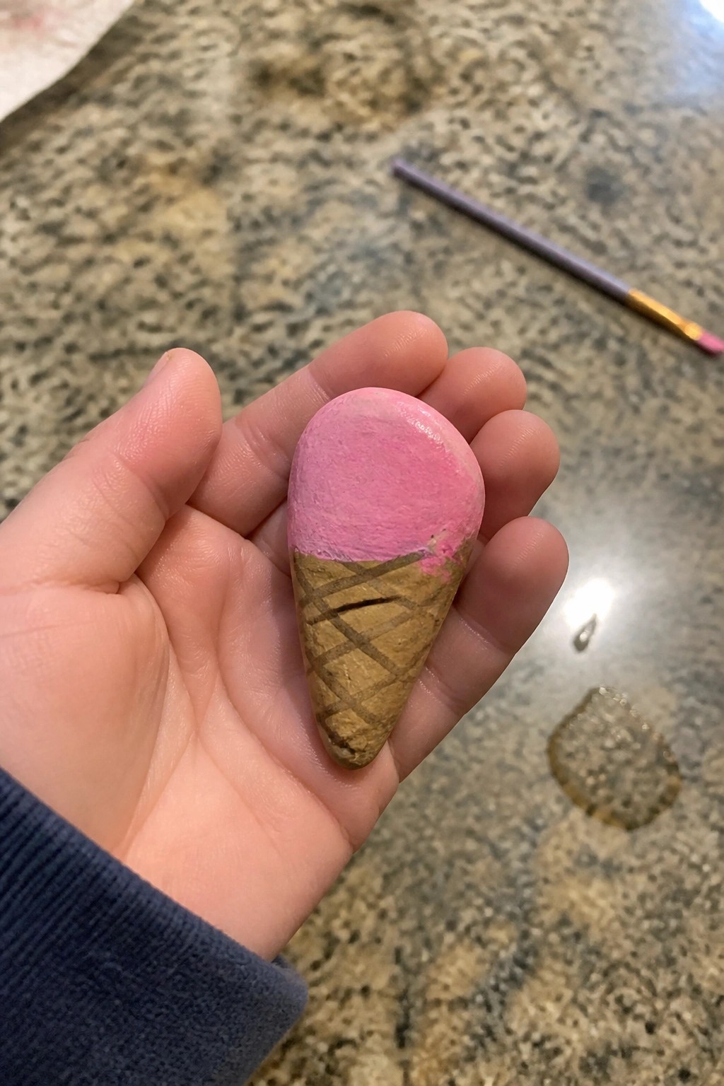 Hand in blue sleeve holding pink ice cream cone painted on stone