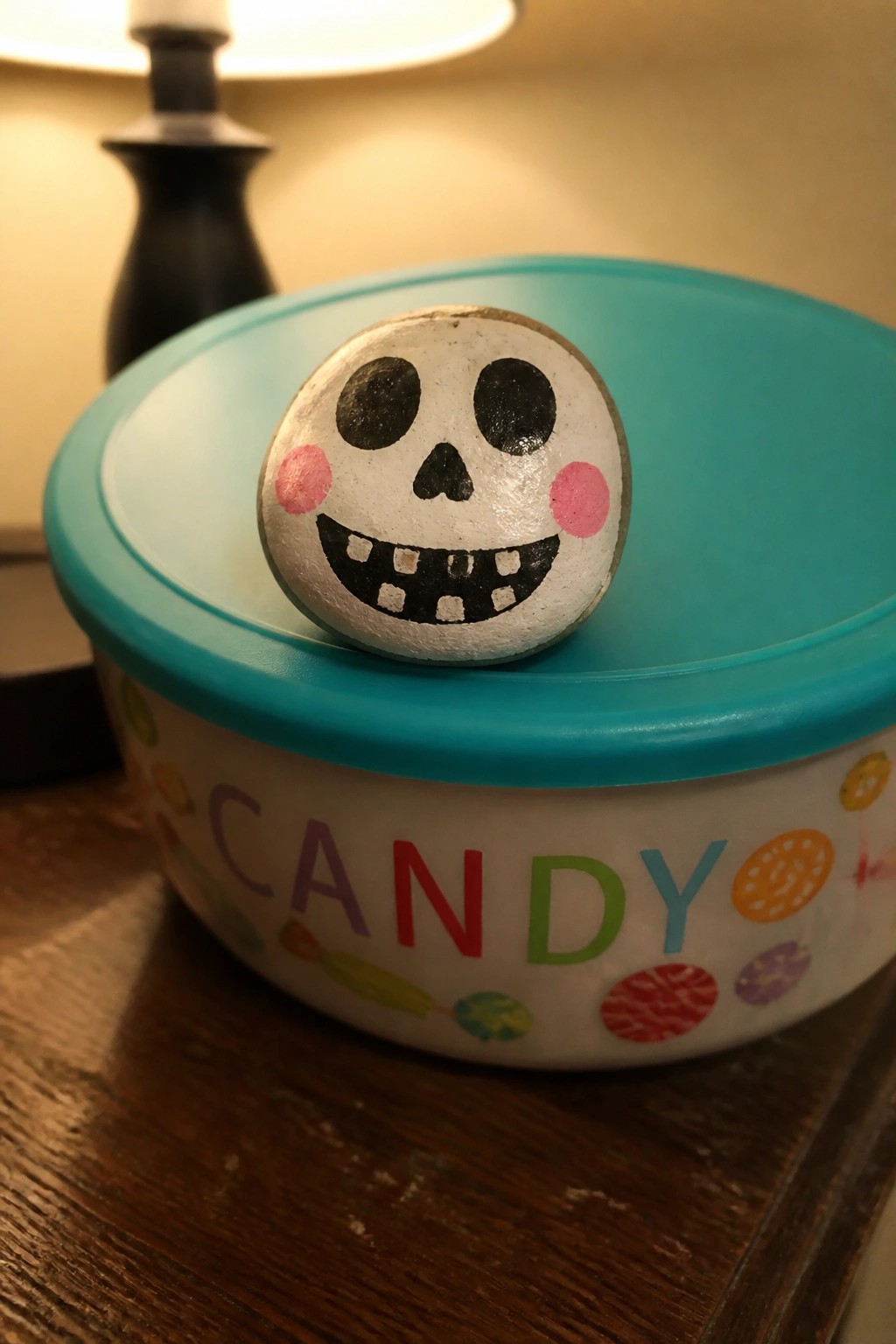 Painted skull rock with pink cheeks atop turquoise candy bowl lid