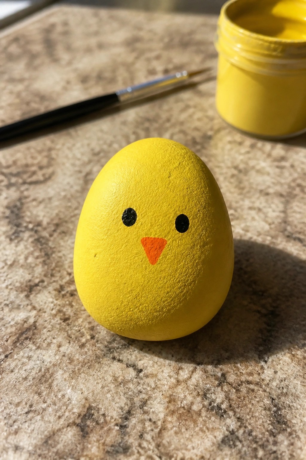 Yellow egg painted as chick with black eyes, orange beak, paint jar nearby.