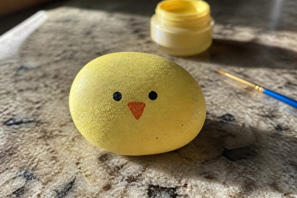 Yellow egg painted as chick with black eyes, orange beak, paint jar nearby.