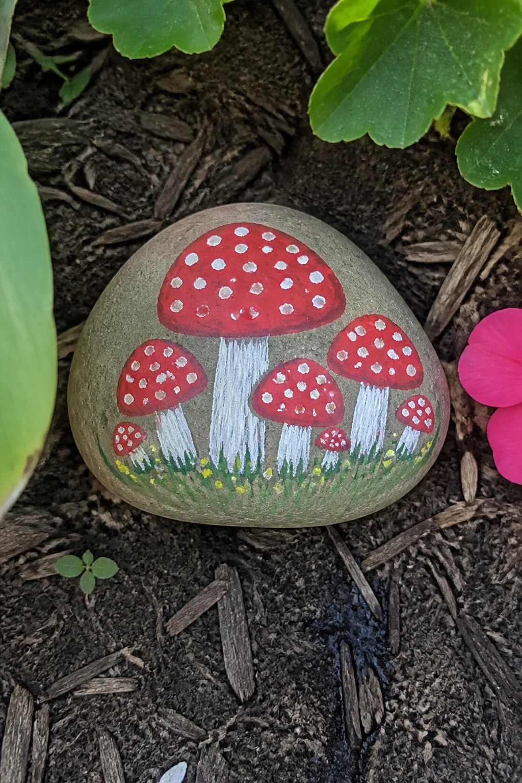 Gray rock painted with red mushrooms dotted white above green grass base