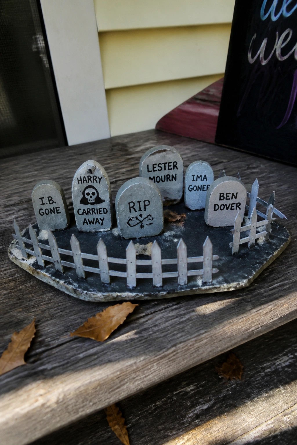 Miniature graveyard with punny tombstones and white picket fence on wood