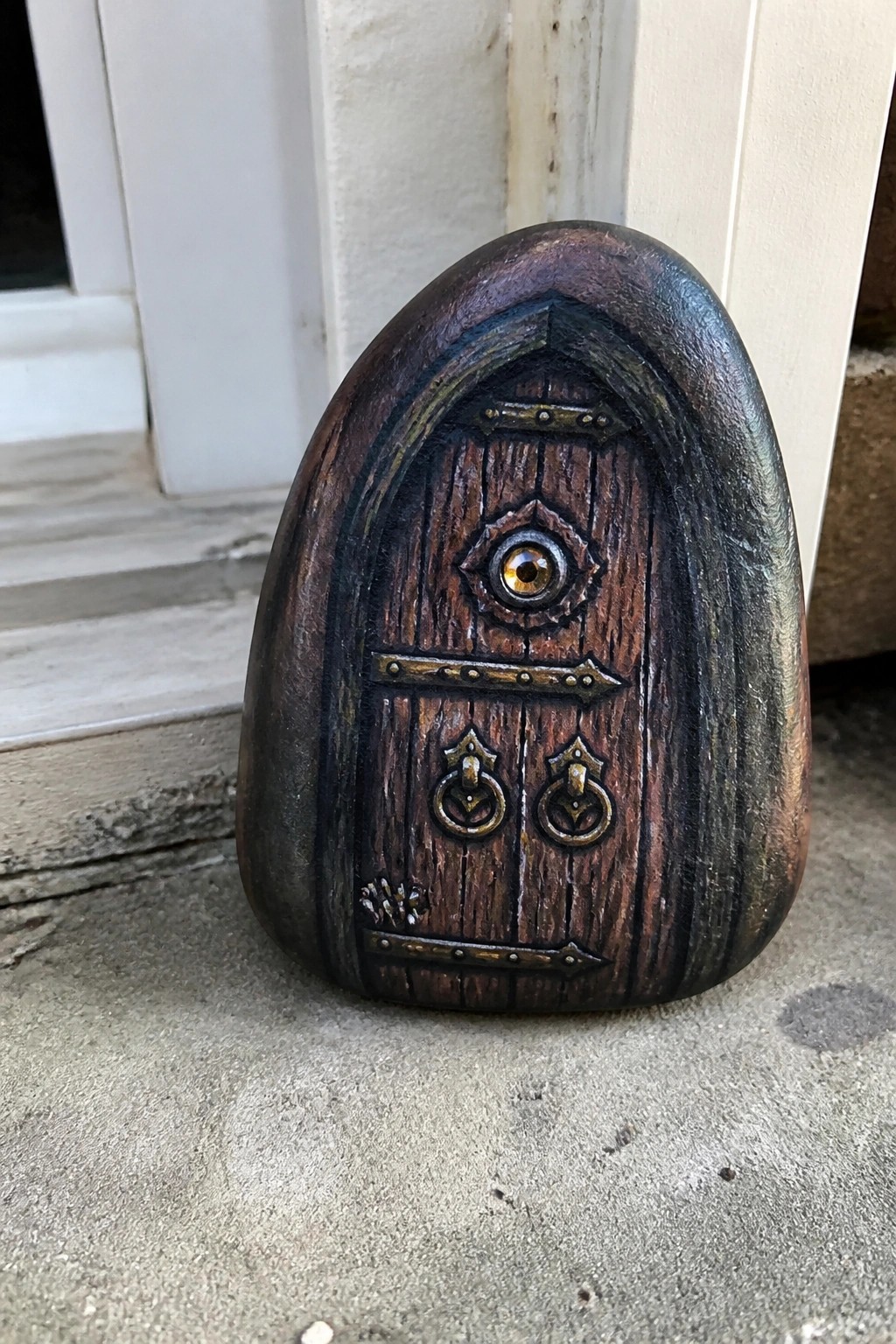 Painted stone shaped as wooden arched door with central eye and brass handles on pavement.