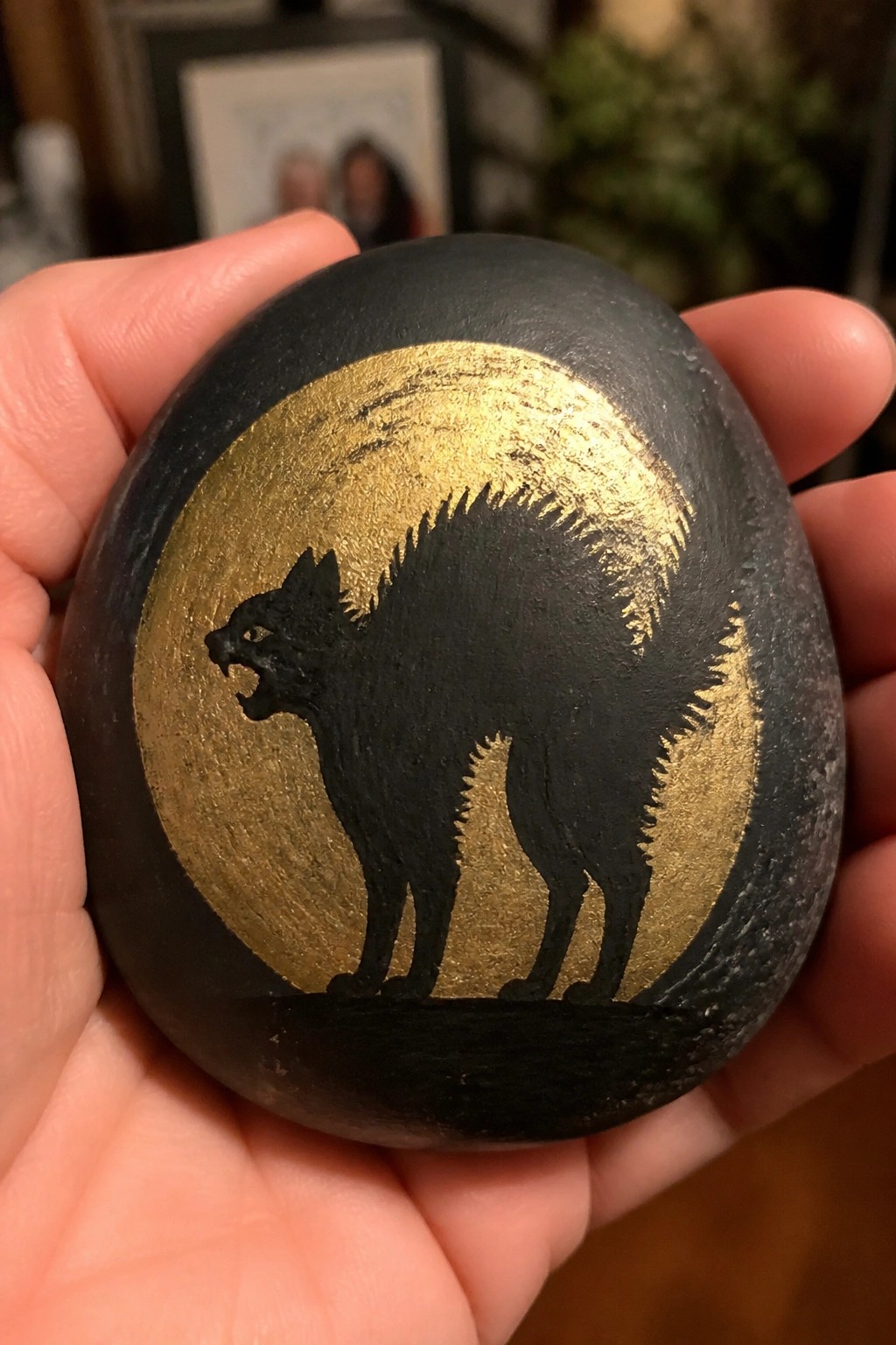 Hand holding black stone with gold moon and arched black cat silhouette