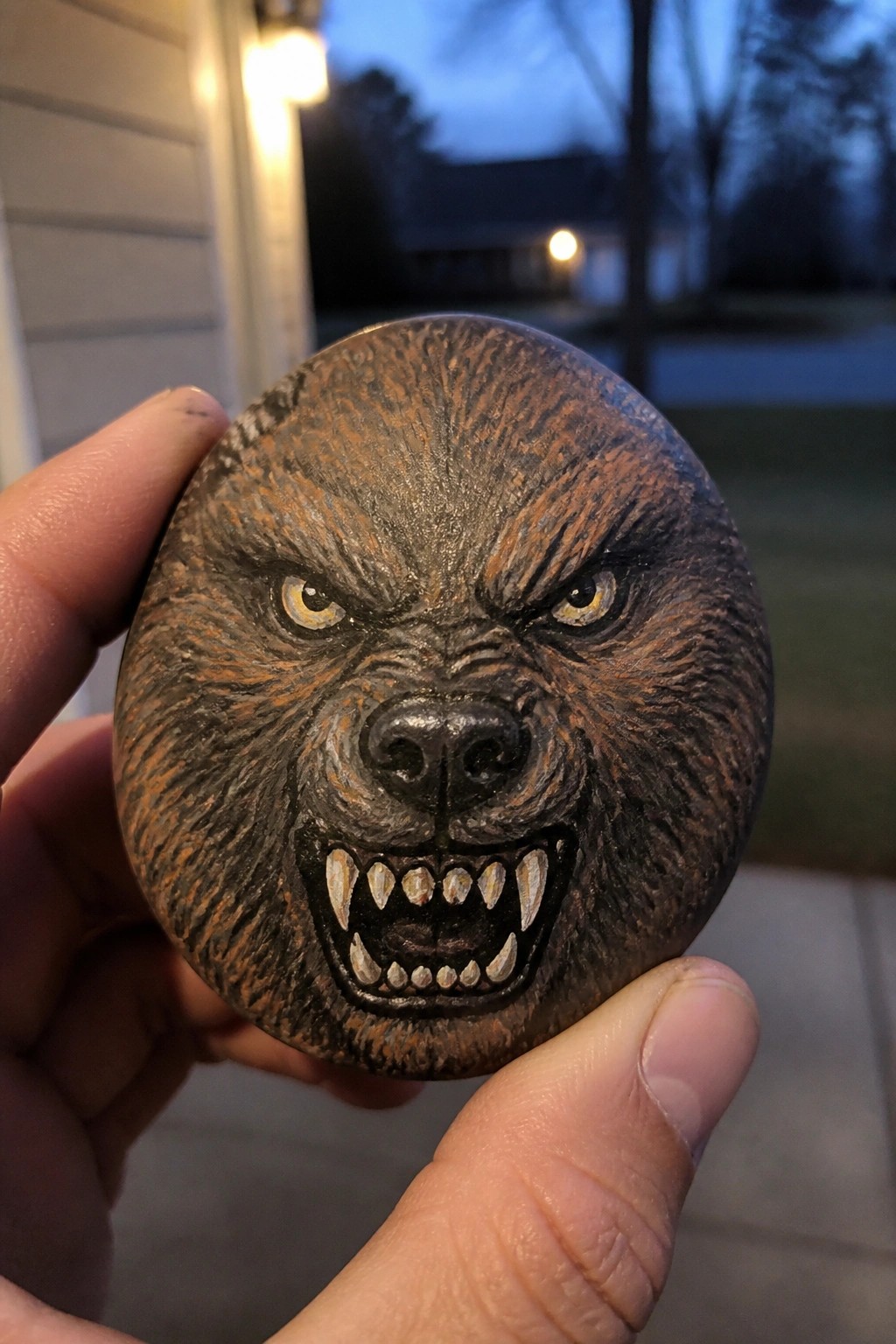 Hand holding painted rock with fierce snarling wolf face and yellow eyes