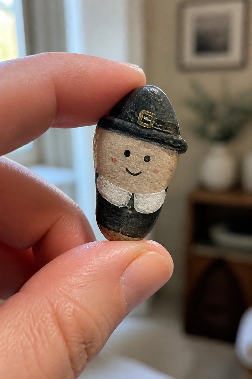 Hand holding painted pebble Pilgrim with black buckled hat and white collar