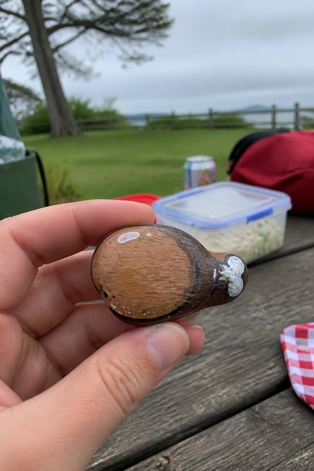 Hand holding small brown wooden bird carving on outdoor picnic table