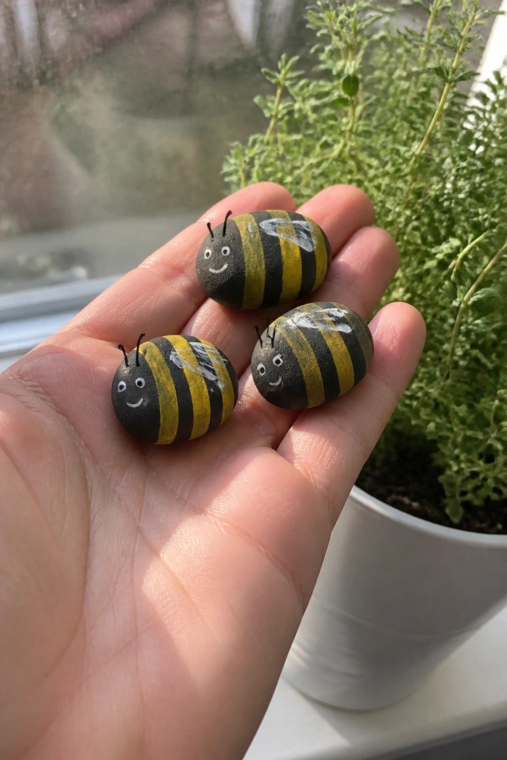 Three black-and-yellow striped bee rocks with faces held in an open palm.