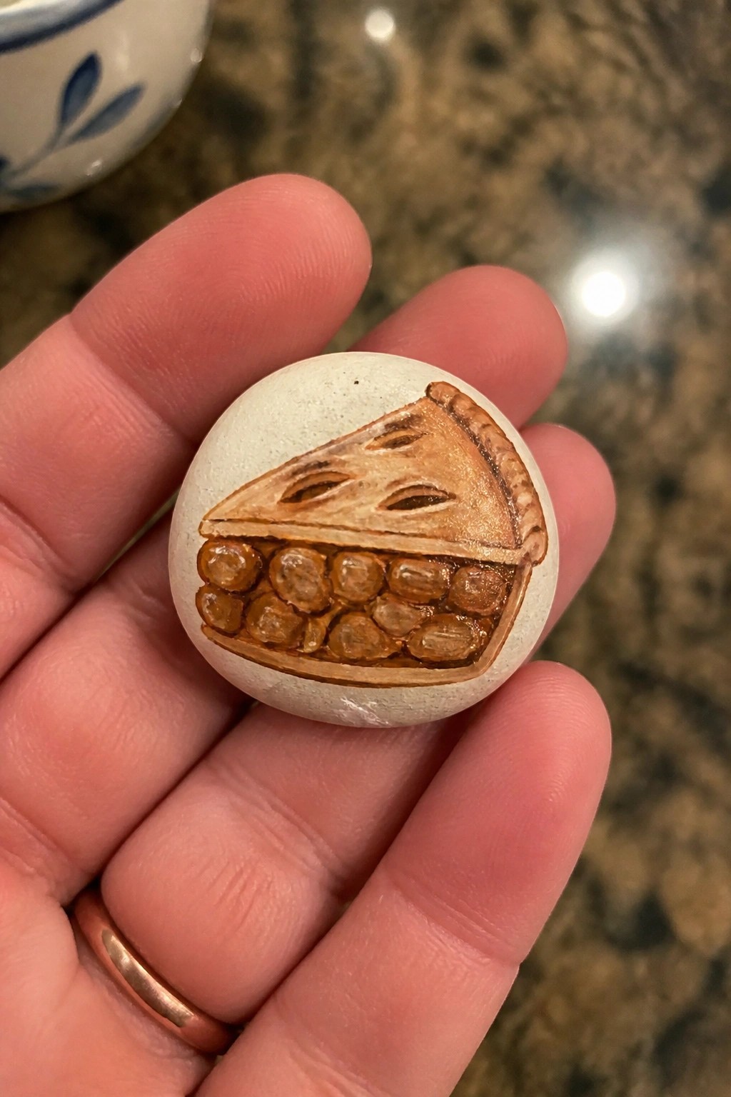 Hand holding painted stone showing slice of pecan pie with crust