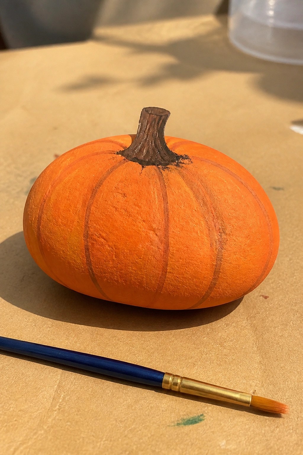 Orange pumpkin with brown stem beside blue paintbrush on brown surface