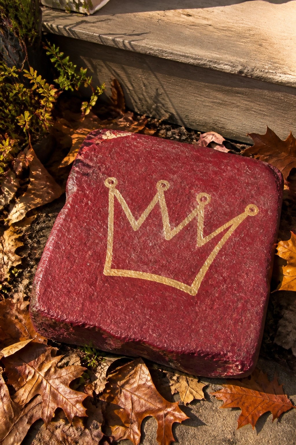 Red brick with gold crown among dry autumn leaves by stone steps