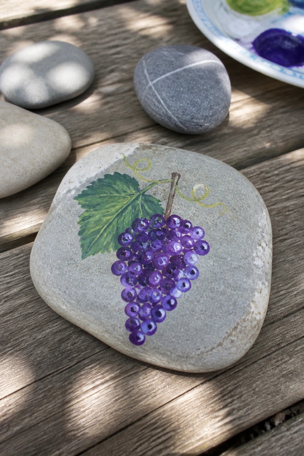Gray stone painted with purple grapes, green leaf on wooden table
