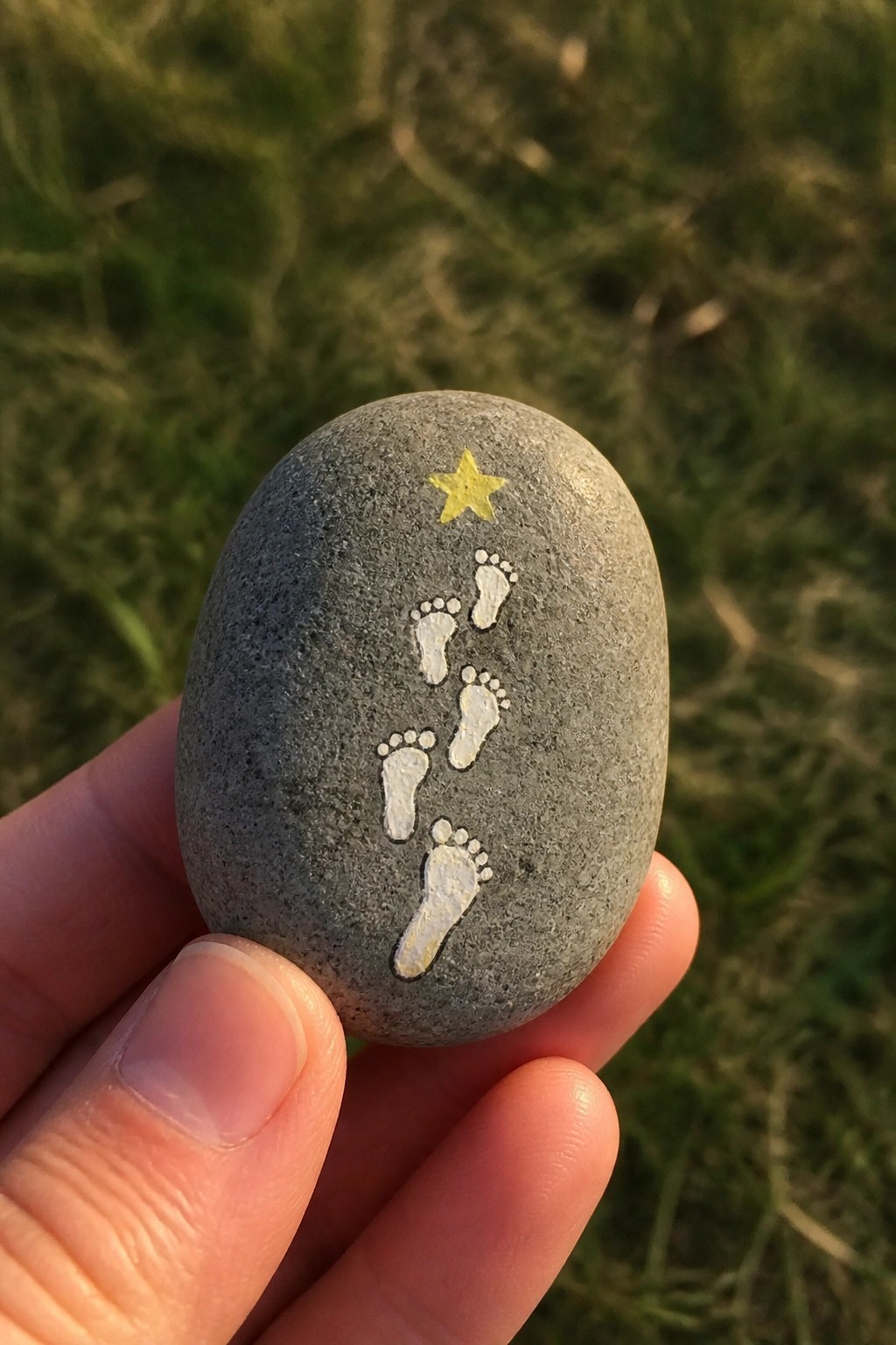 Hand holding gray stone with white footprints leading to yellow star