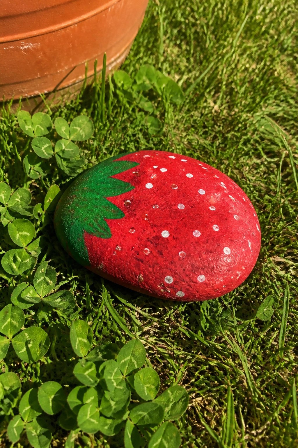 Painted red strawberry rock with white dots and green leaves on grass