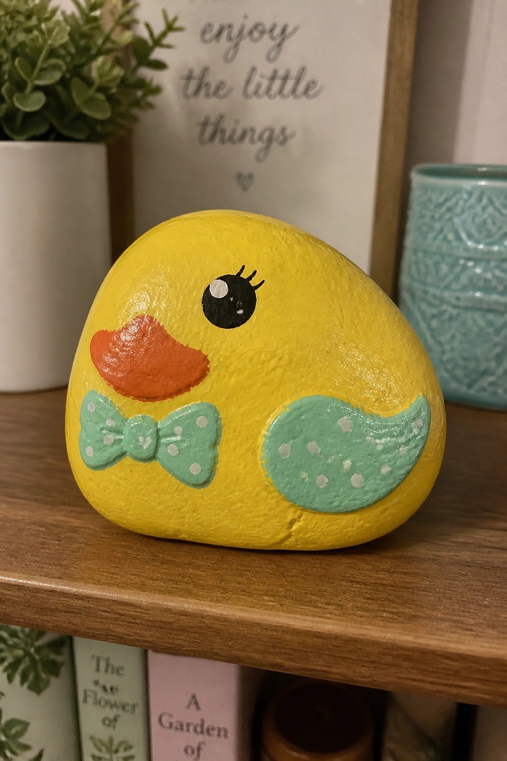 Yellow painted duck rock with orange beak, polka-dotted mint bow and wing on shelf
