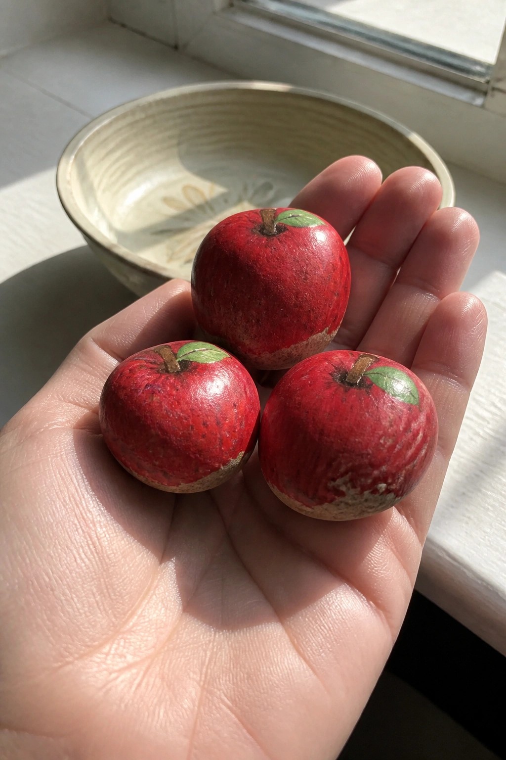 Hand holding three small painted red apples with green leaves and stems