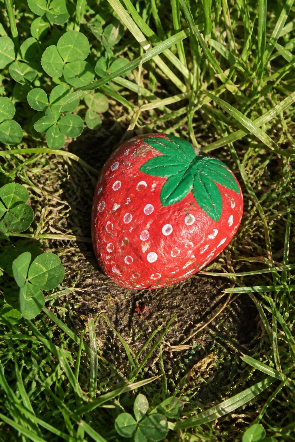 Red painted strawberry rock with white dots and green leaves on grass