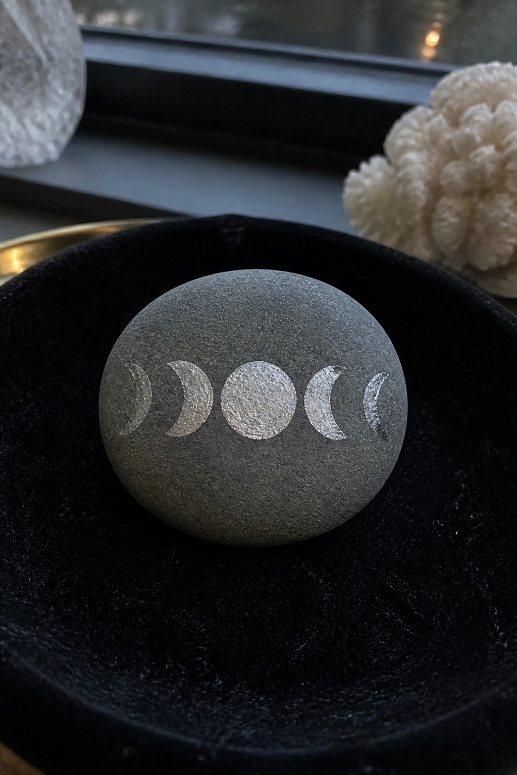 Gray stone engraved with silver moon phases in black velvet bowl