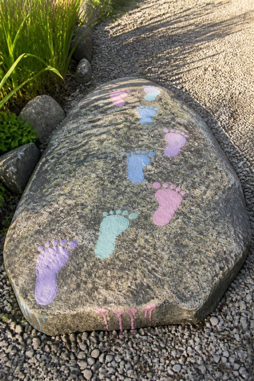 Large rock with colorful painted footprints in purple, blue, and pink on gravel